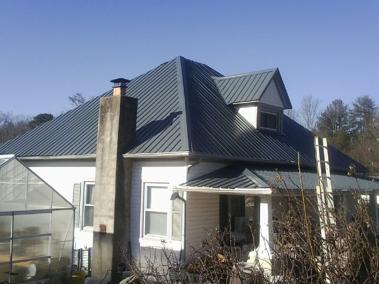 Dark blue standing seam metal roof on a white farmhouse with dormer — Slate & Tile Roof Repair by Roofing Brothers in Orange Lake