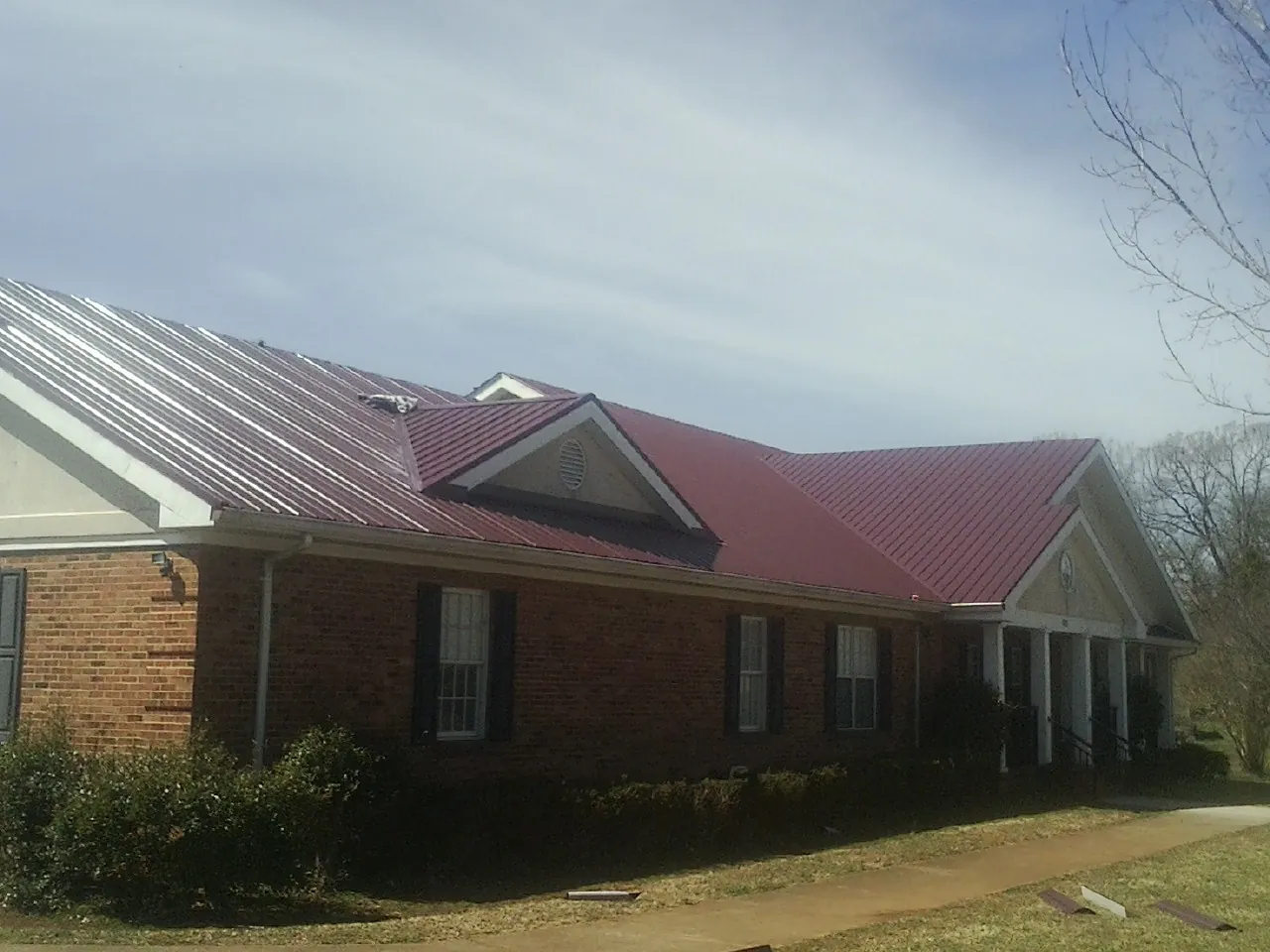 Red metal roof with gabled entries on a long brick building, from a Hail Damage Roof Repair job in Orange Lake