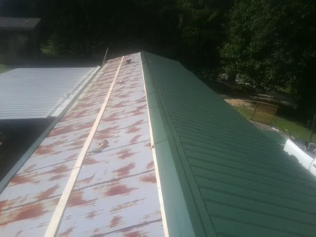 Old rusted panels beside newly installed green metal roofing — Wind Damage Roof Repair by Roofing Brothers in Orange Lake