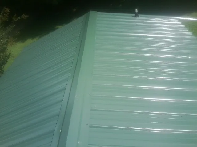 New green metal panels meeting at the ridge of a roof — Flat Roof Repair work by our crew in Orange Lake