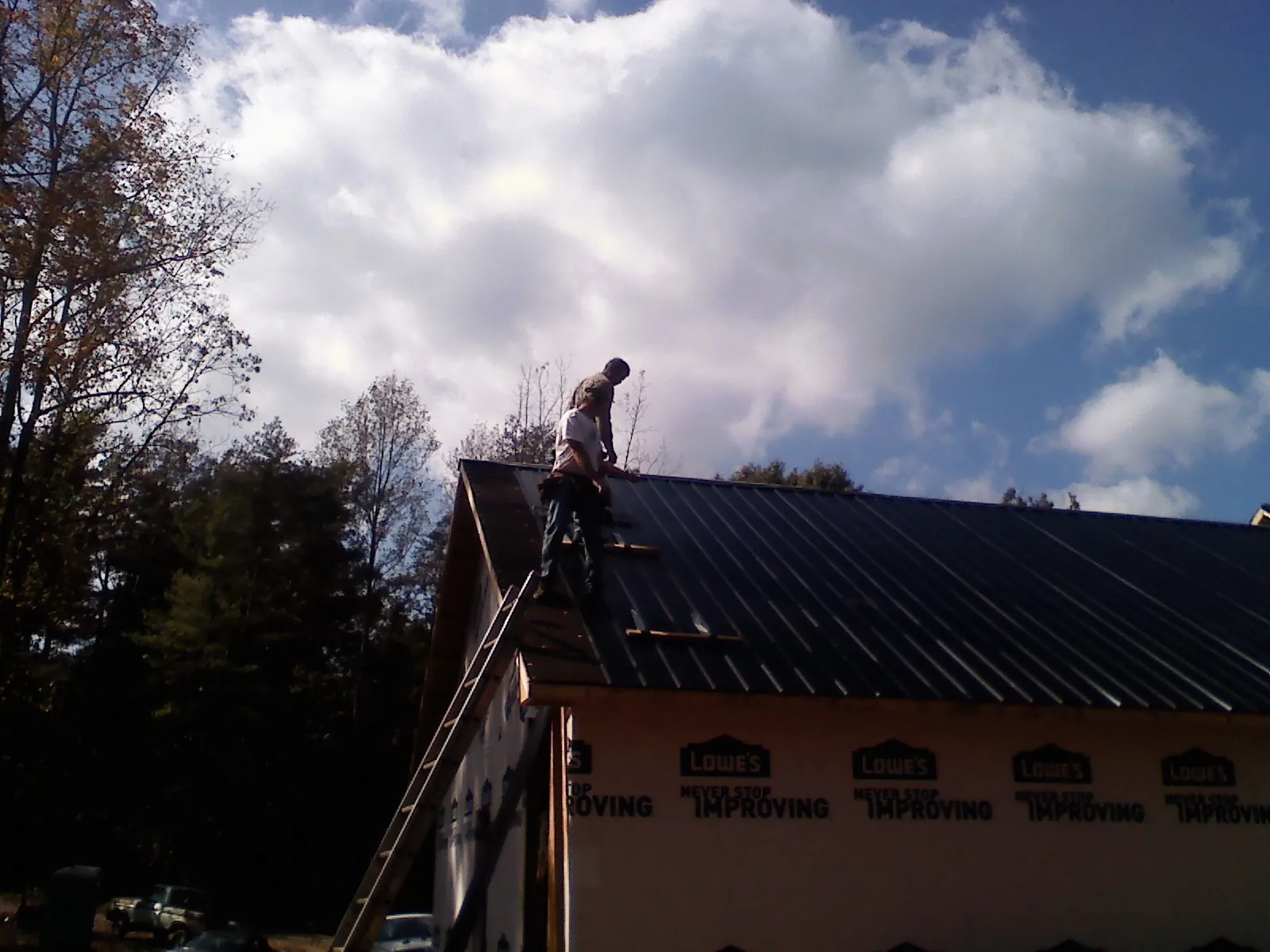 Roofer fastening dark metal panels high against a cloudy sky, from a Roof Inspection job in Orange Lake