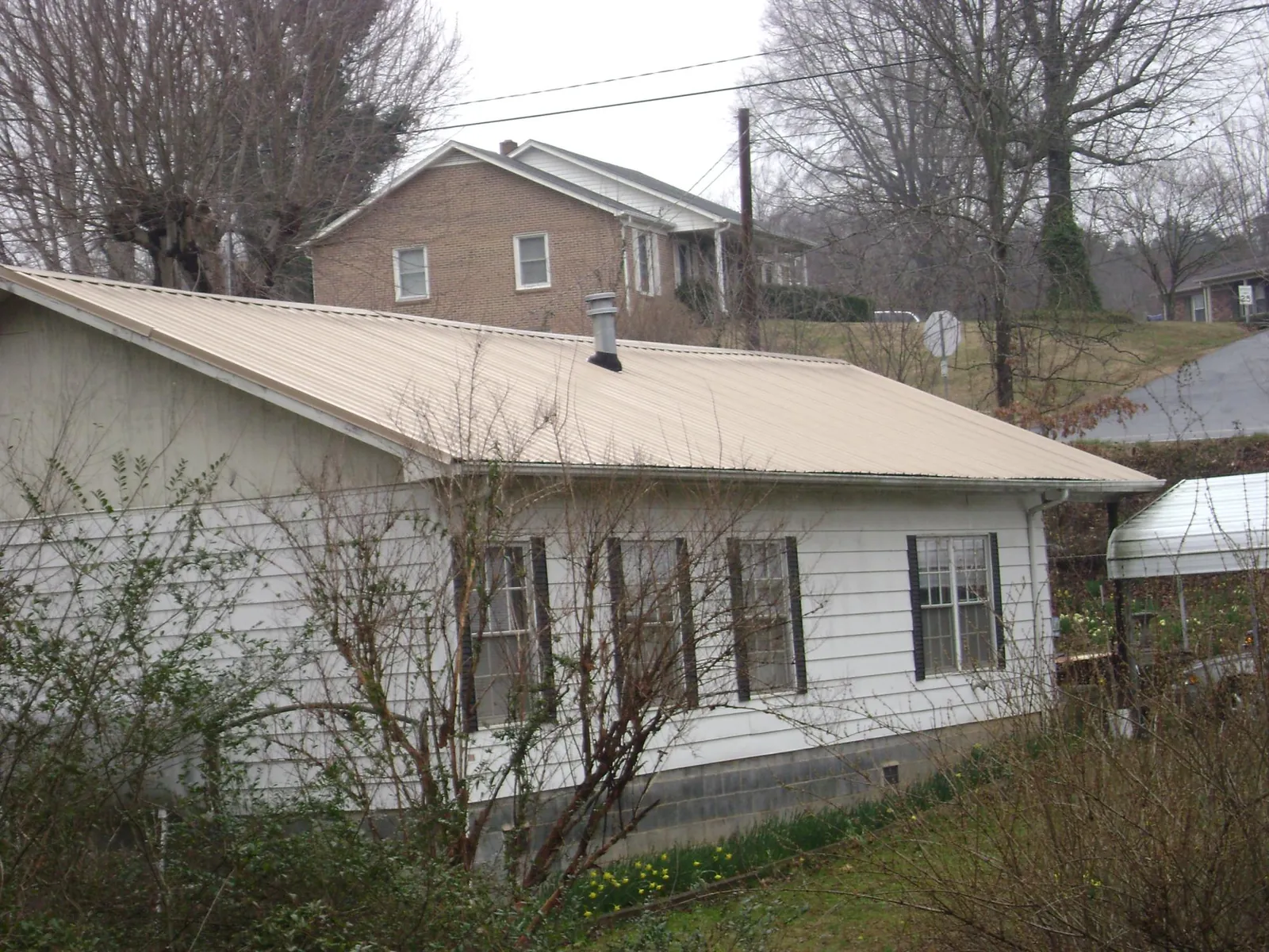 Tan metal roof on a white sided house set into a hillside — Commercial Roofing by Roofing Brothers in Orange Lake