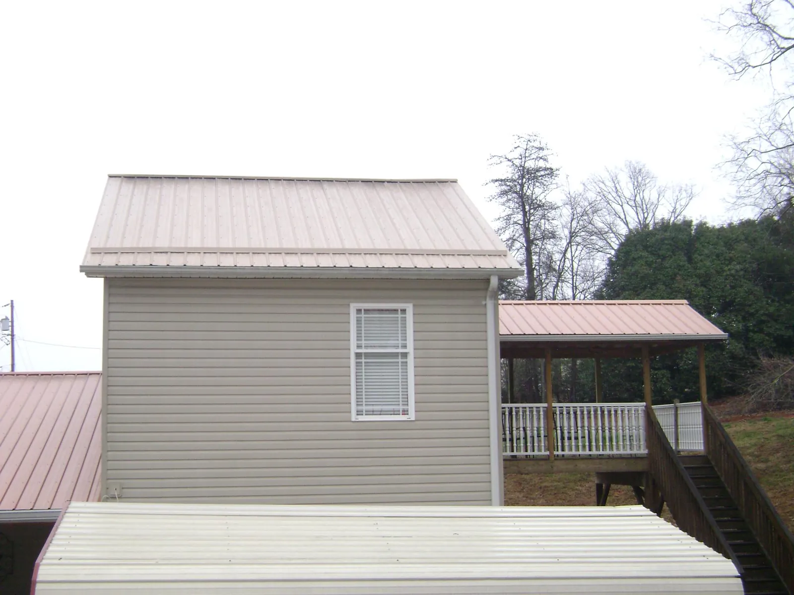 Tan metal roofs on a two story addition and attached porch, from a Roof Replacement job in Orange Lake